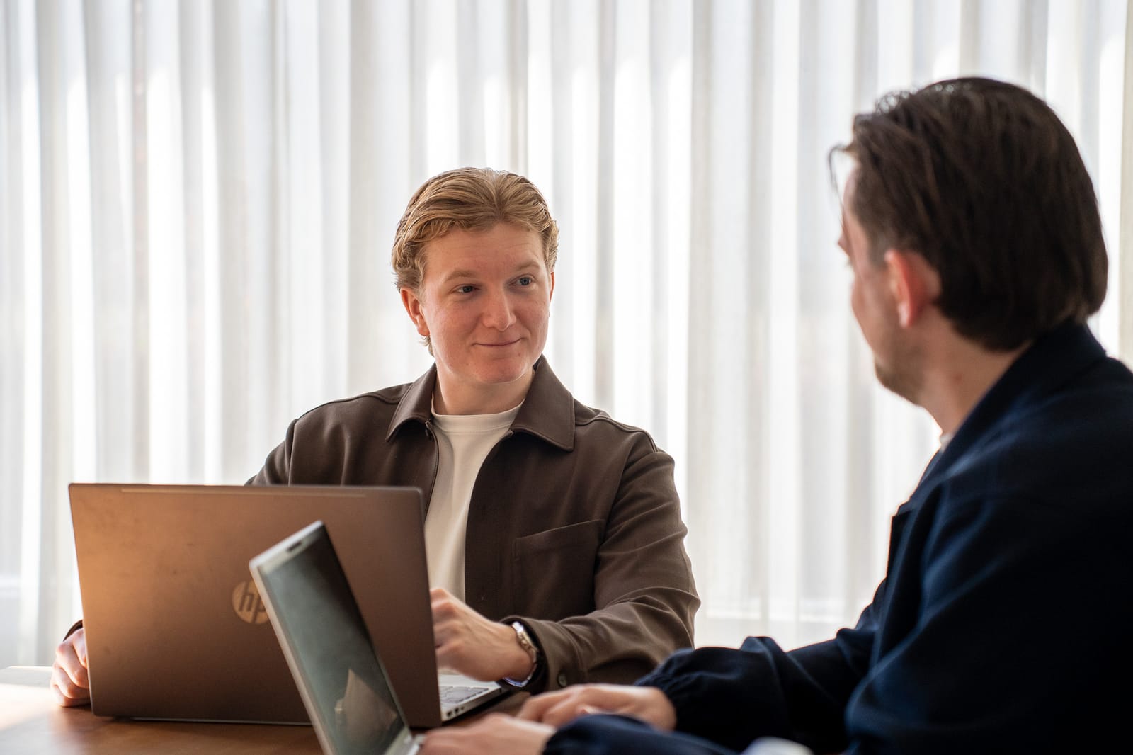 Twee collega's van SENT Marketing in overleg aan tafel achter hun laptops