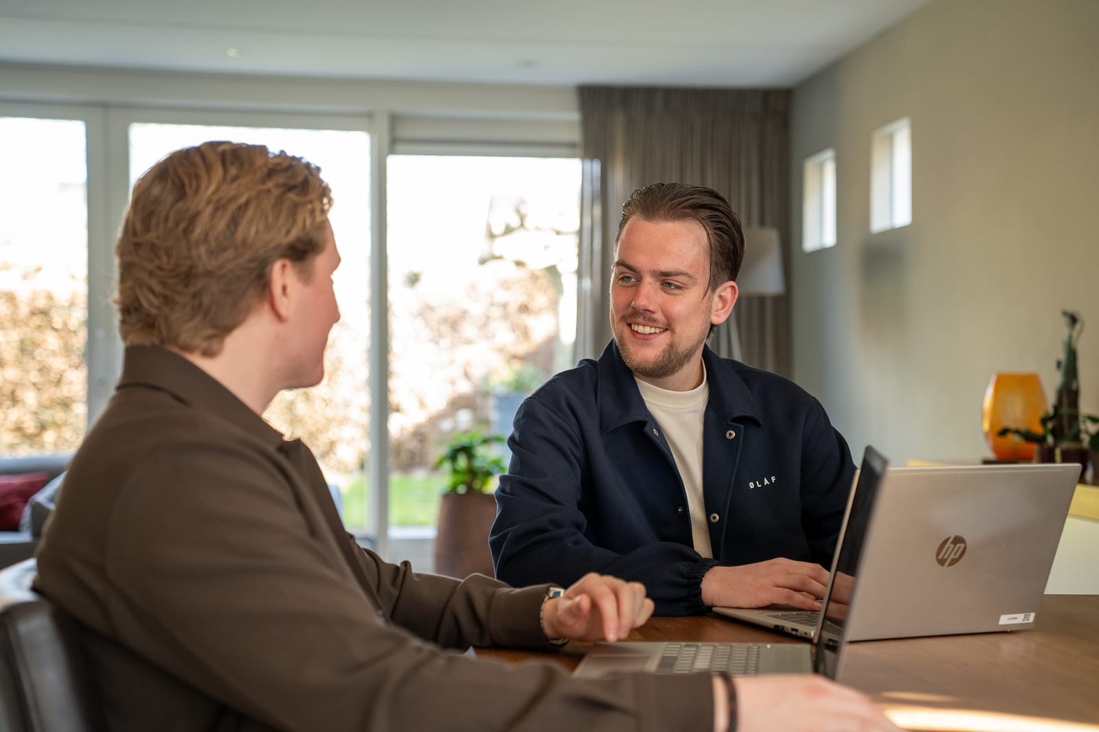 Twee collega's van SENT Marketing in gesprek aan een tafel met laptops in een lichte woonkamer