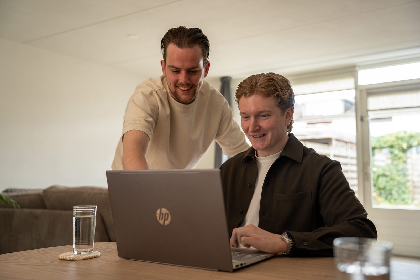 Twee collega's van SENT Marketing kijken lachend samen naar een laptop aan tafel